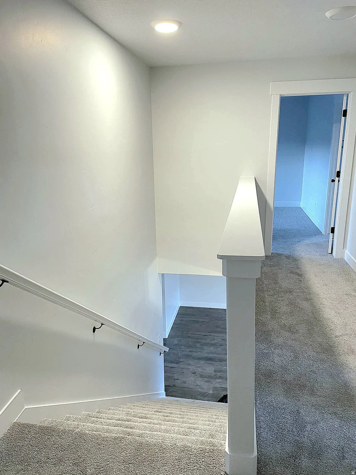 Carpeted stairway with a contrasting wood-finish landing below, featuring a white handrail and recessed lighting