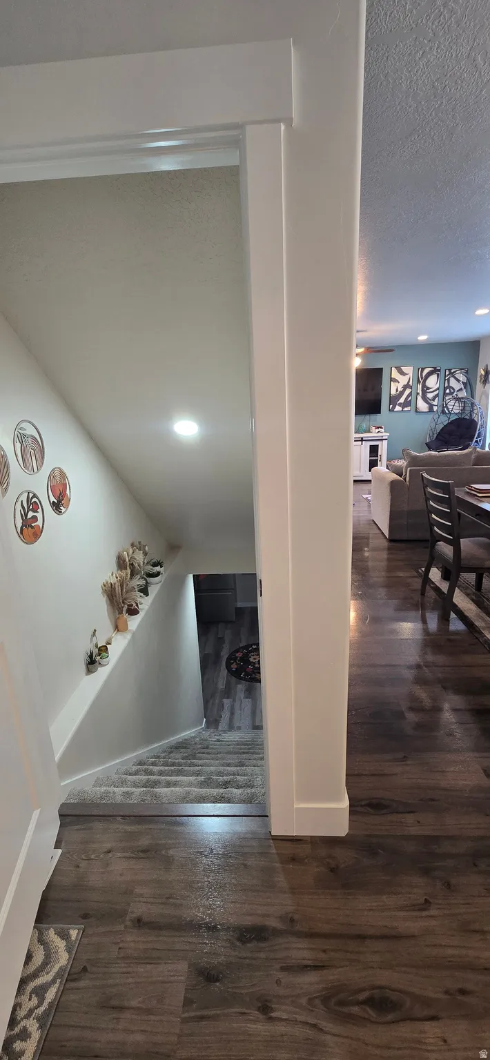 Wood-finish flooring throughout a hallway leading to a carpeted staircase with recessed lighting