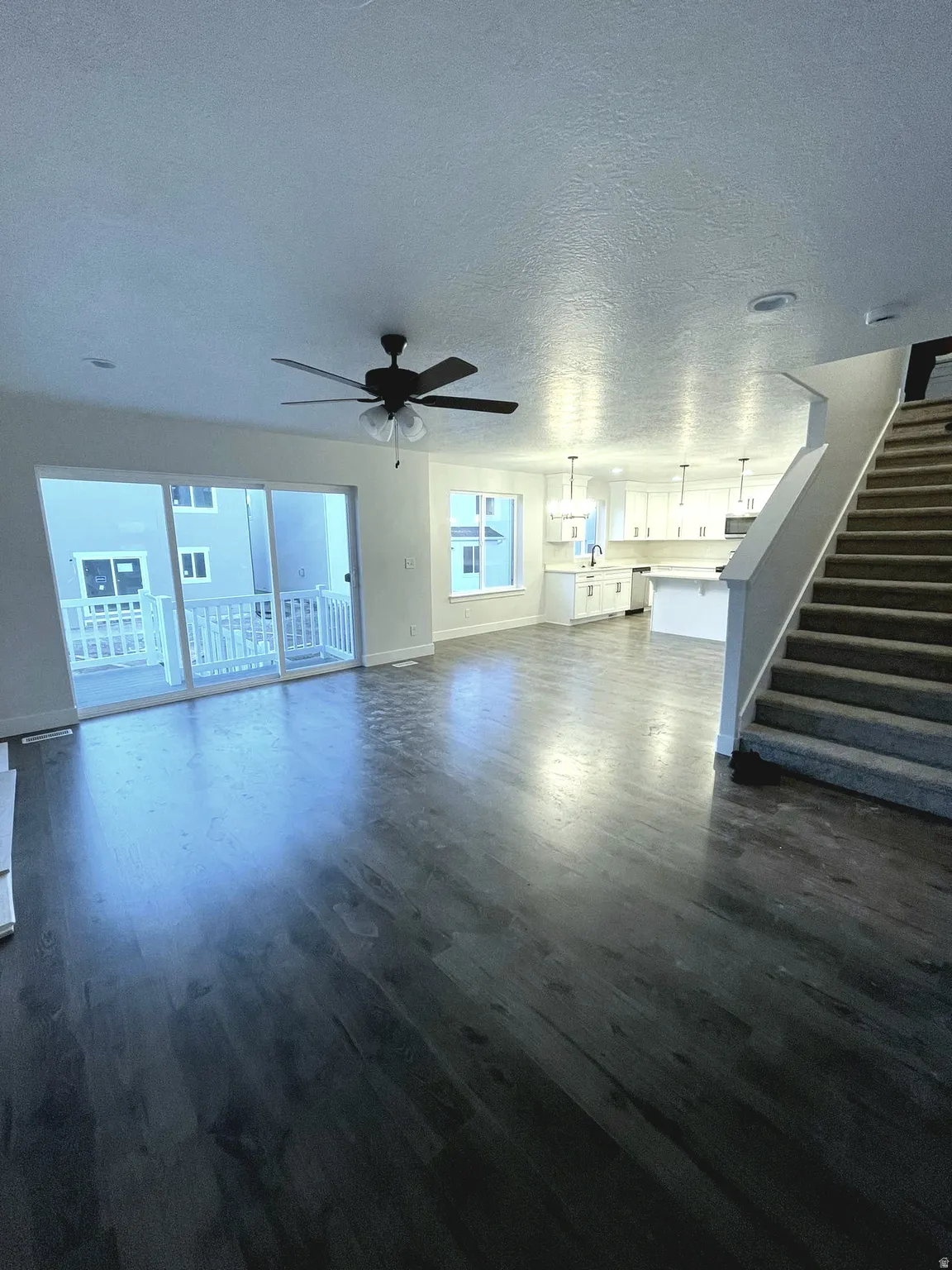 Spacious living area featuring dark wood-finish flooring, a contemporary ceiling fan, and sliding glass doors to an exterior balcony