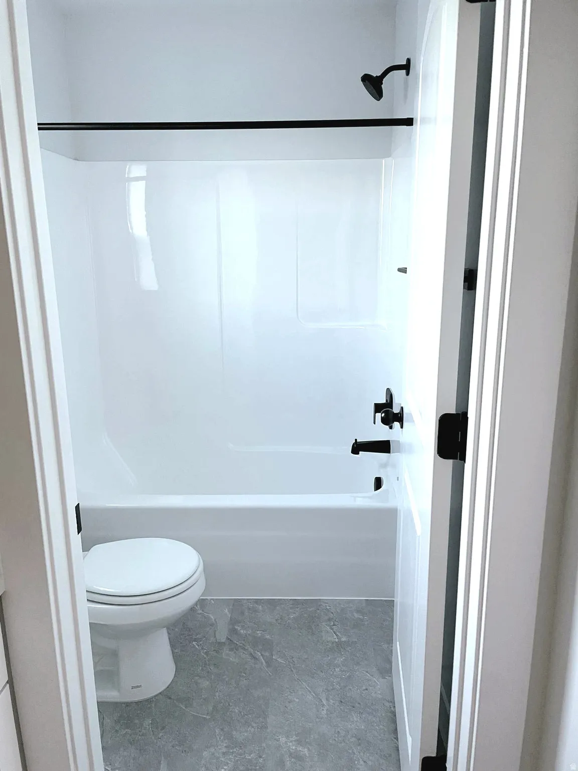 Bathroom featuring a white tub/shower combination with matte black fixtures, white toilet, and gray stone-finish flooring
