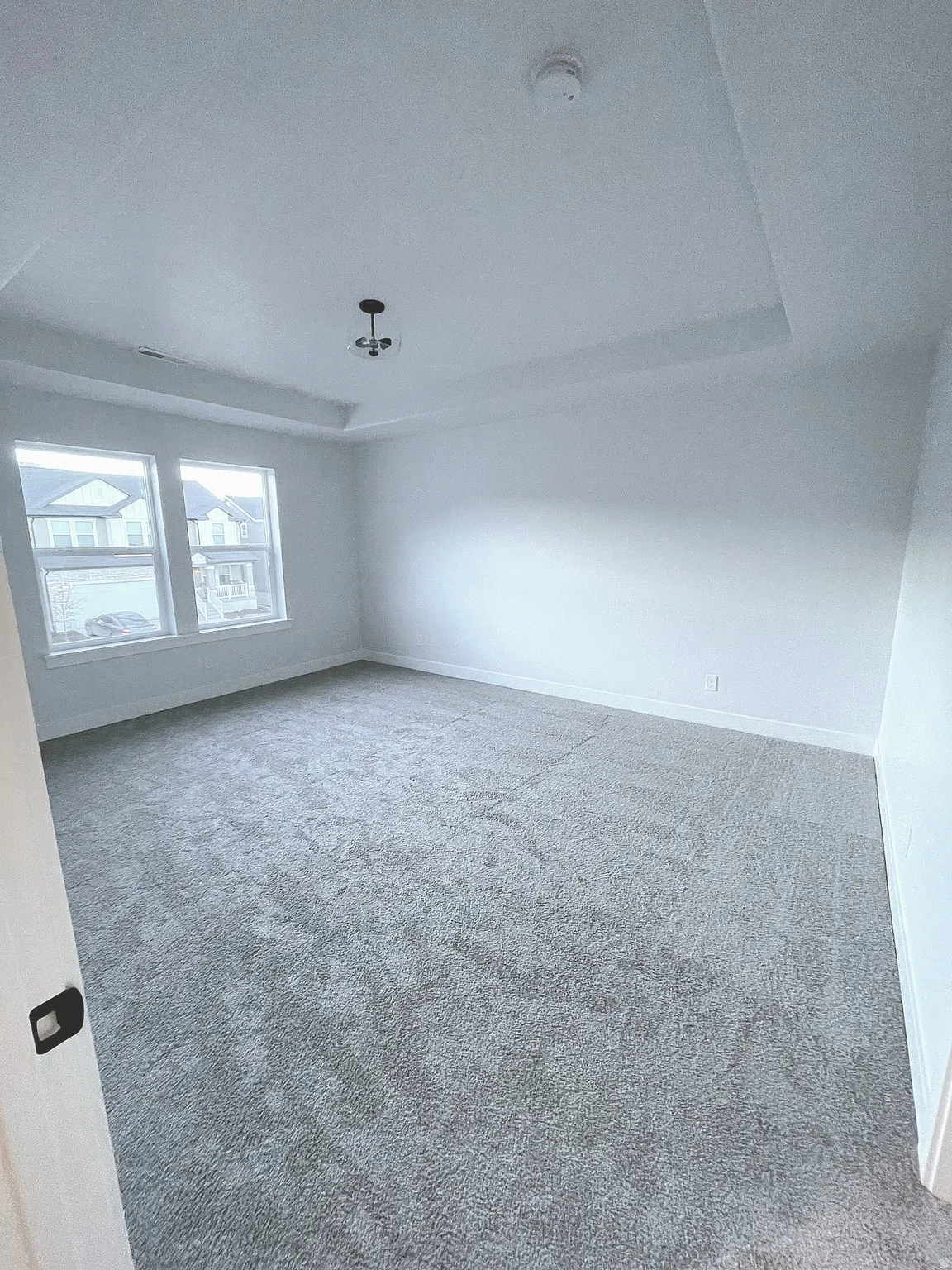 Spacious room featuring light gray carpeting, neutral wall finishes, and a tray ceiling with a central lighting fixture