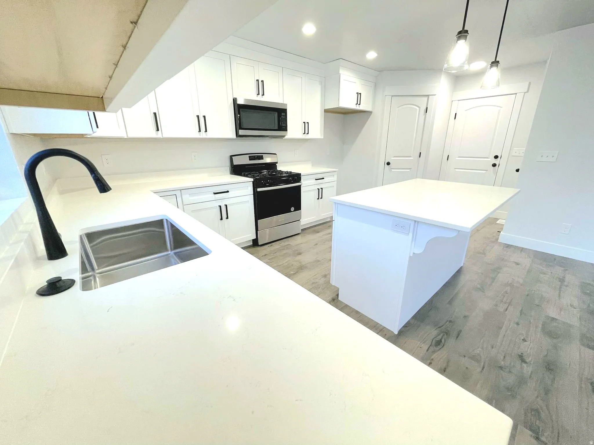 Modern kitchen featuring white cabinetry with matte black hardware, light-toned countertops, wood-finish flooring, a stainless steel gas range, and a built-in microwave
