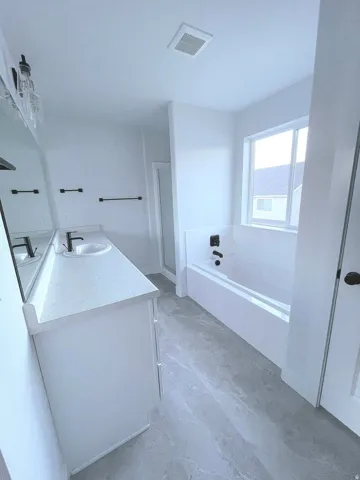 Contemporary bathroom featuring a double vanity with white cabinetry and light-toned countertops, a built-in tub with dark fixtures, a separate glass-enclosed shower, and light gray tile flooring