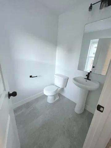 Pedestal sink with a matte black faucet, white toilet, and large rectangular wall mirror