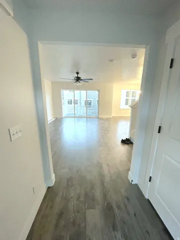 Open-concept living space featuring wood-finish flooring, a ceiling fan, and large glass sliding doors leading to a private balcony