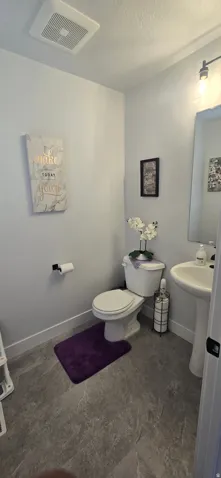 Bathroom featuring a pedestal sink, toilet, gray large-format tile flooring, white baseboards, and a ceiling-mounted ventilation fan