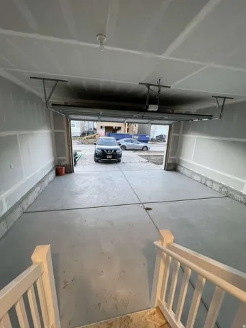 Spacious garage with concrete flooring, unfinished drywall, and a visible garage door opener mechanism
