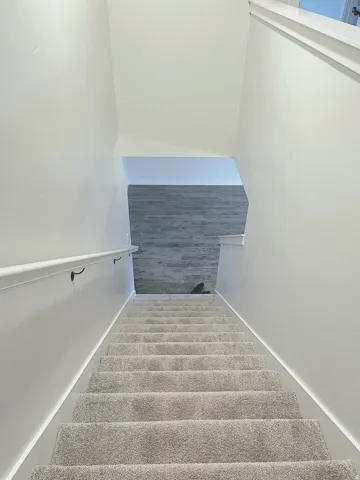 Carpeted staircase with a white handrail, leading to a space with wood-finish flooring and light-toned walls