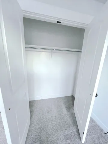 Full-size closet featuring bi-fold panel doors, upper shelf, and clothes hanging rod