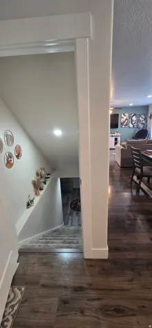 Wood-finish flooring throughout a hallway leading to a carpeted staircase with recessed lighting