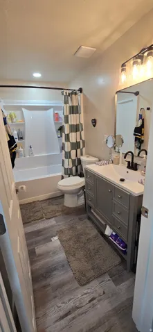 Bathroom with wood-finish flooring, a white vanity with an integrated sink, a dark-toned faucet, and a shower-tub combination