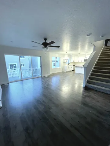Spacious living area featuring dark wood-finish flooring, a contemporary ceiling fan, and sliding glass doors to an exterior balcony