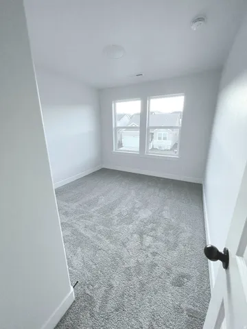 Room featuring plush gray carpeting, white walls, and two large windows