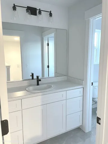 Modern bathroom vanity featuring white shaker cabinetry, a light-toned countertop, and a black-finish faucet