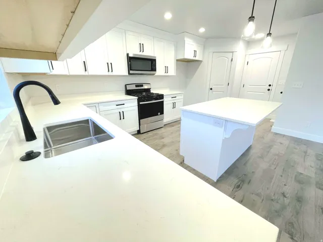 Modern kitchen featuring white cabinetry with matte black hardware, light-toned countertops, wood-finish flooring, a stainless steel gas range, and a built-in microwave