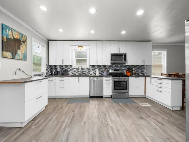 Contemporary kitchen featuring white cabinetry, stainless steel appliances, a mosaic tile backsplash, dark countertops, and wood-finish flooring
