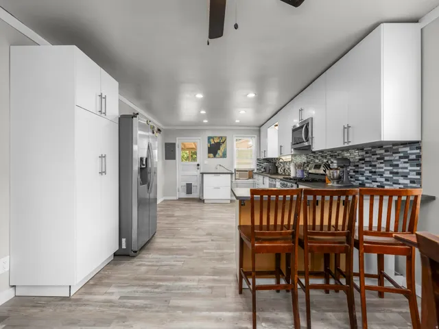 Contemporary kitchen featuring abundant white cabinetry, integrated stainless steel appliances, a mosaic tile backsplash, and wood-finish flooring