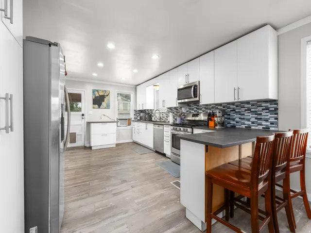 Modern kitchen featuring stainless steel appliances, white cabinetry, a multi-tone tile backsplash, and light wood-finish flooring