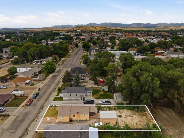 Aerial perspective featuring a property boundary encompassing a residential structure with a light-colored exterior, a detached garage, and an expansive undeveloped lot