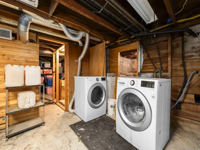 Laundry area featuring two front-loading machines, exposed wooden beam ceiling, and concrete flooring
