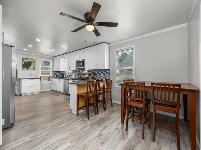 Modern kitchen featuring white cabinetry, stainless steel appliances, a mosaic tile backsplash, and light wood-finish flooring