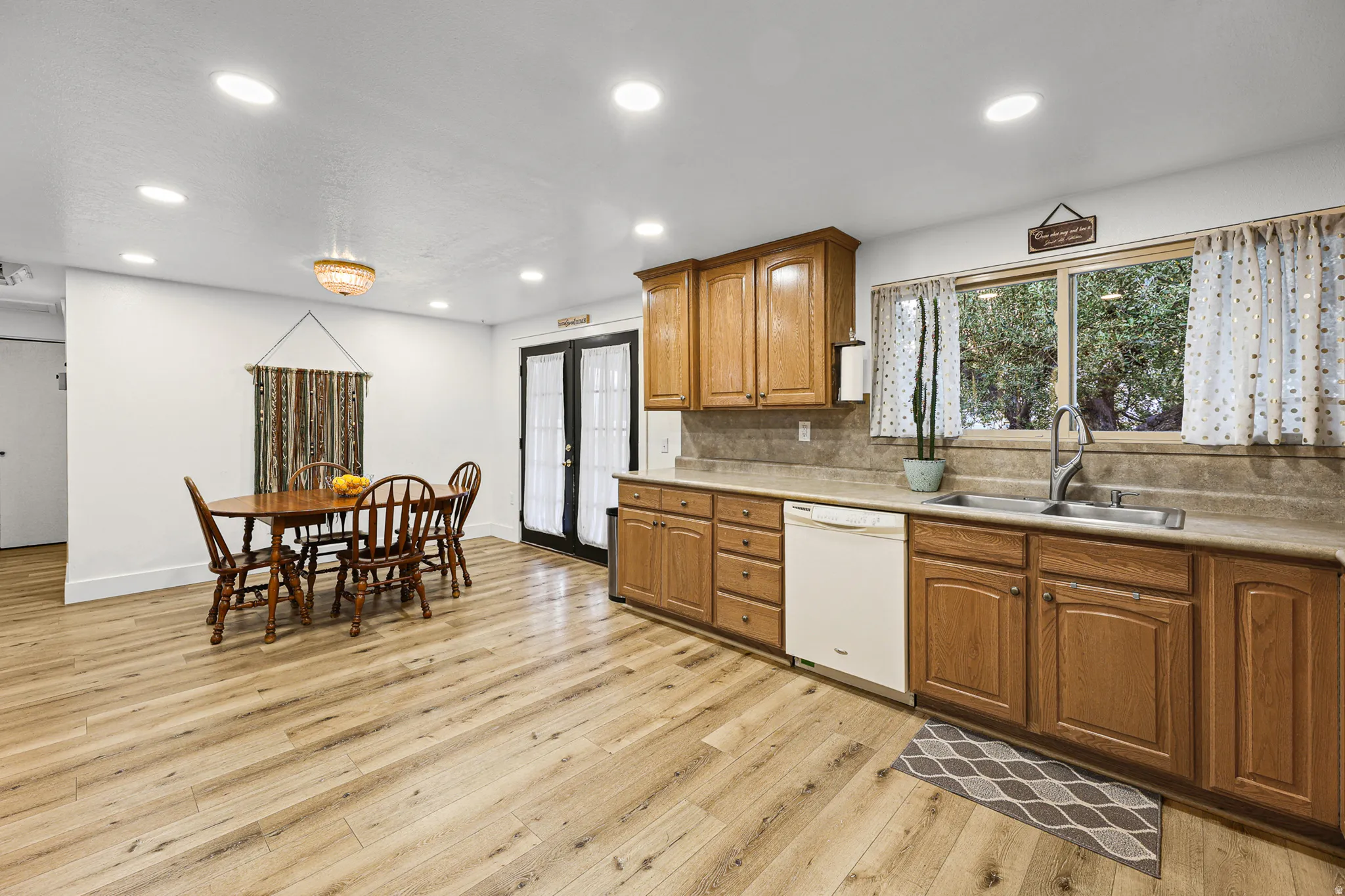Open-concept kitchen and dining area featuring wood-finish flooring, recessed lighting, and a kitchen window overlooking mature trees