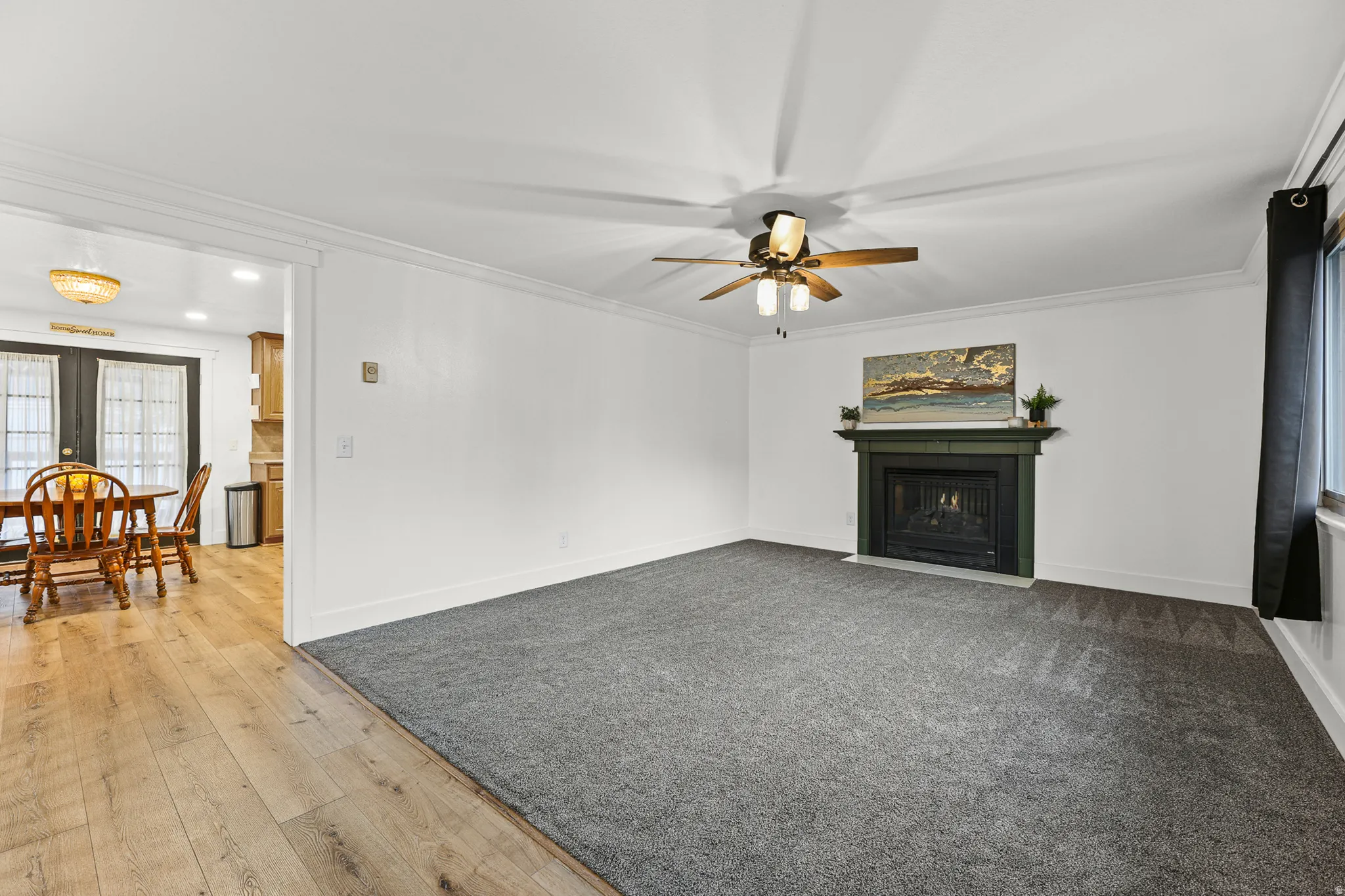 Spacious living area featuring a central fireplace with a dark mantel, crown molding, and a ceiling fan