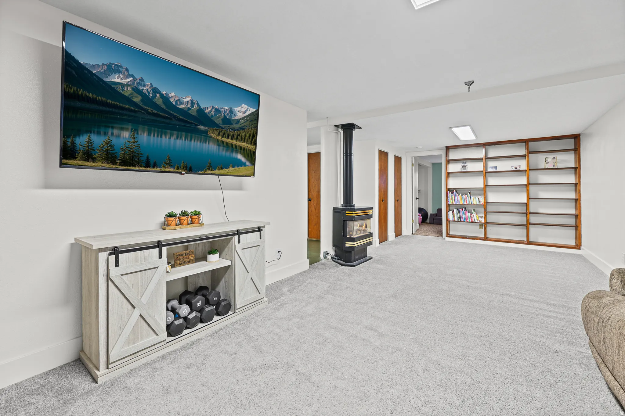 Spacious room featuring light gray carpeting, built-in shelving, a freestanding wood-burning stove, and a recessed ceiling light