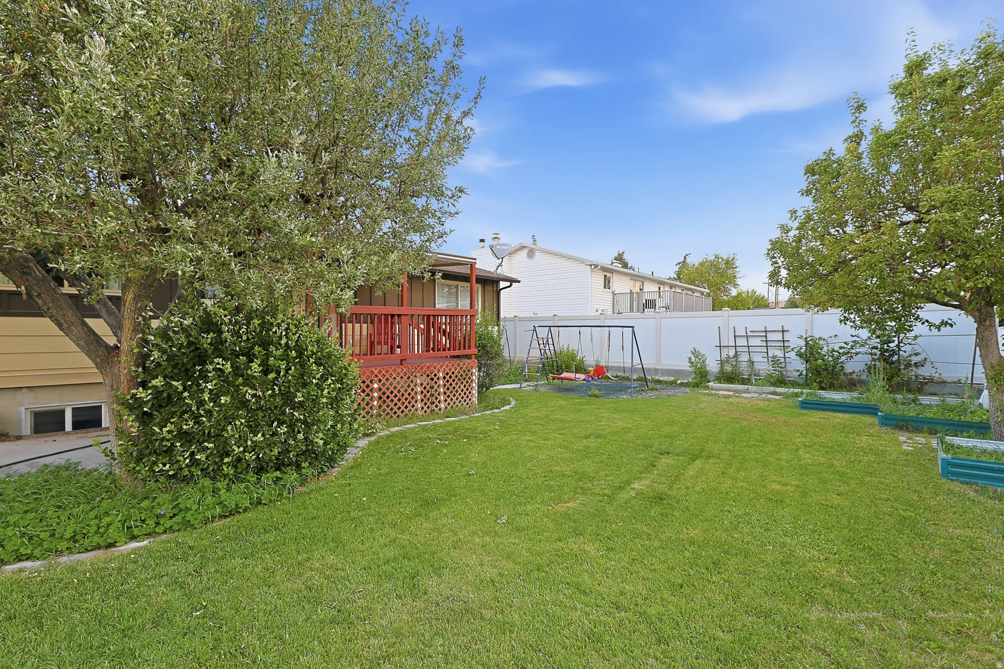 Spacious backyard featuring a manicured lawn, mature trees, and a raised wooden deck with lattice detailing