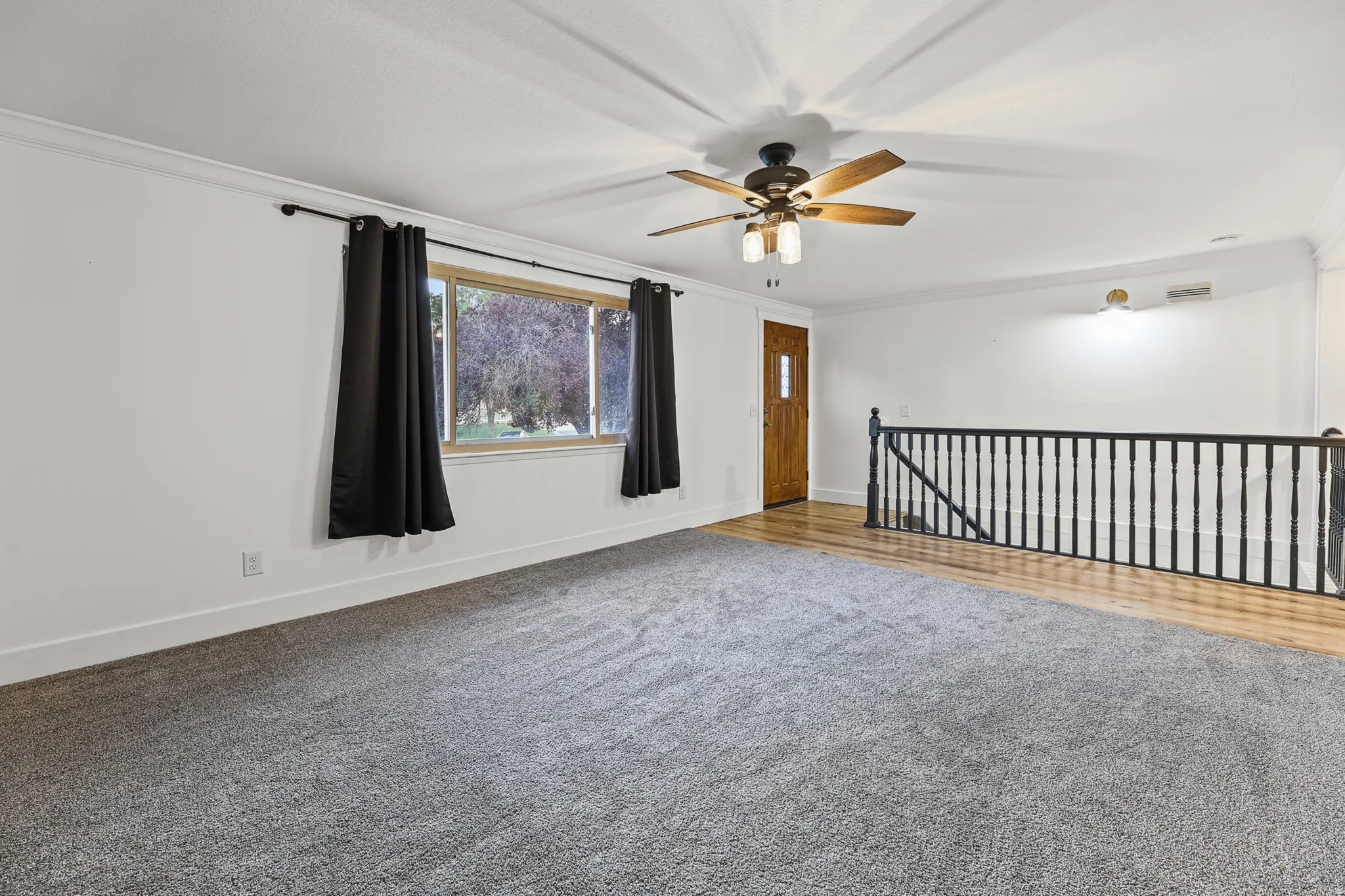 Spacious living area featuring newer gray carpeting, crown molding, and a ceiling fan