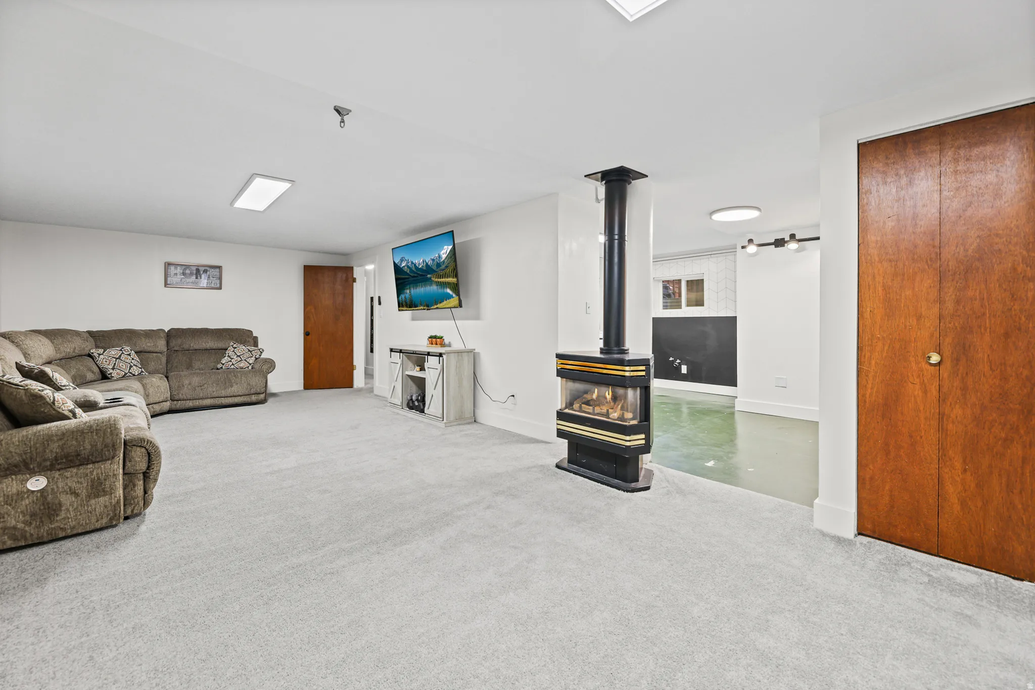 Spacious carpeted room featuring a freestanding fireplace with a black and gold finish, and recessed lighting