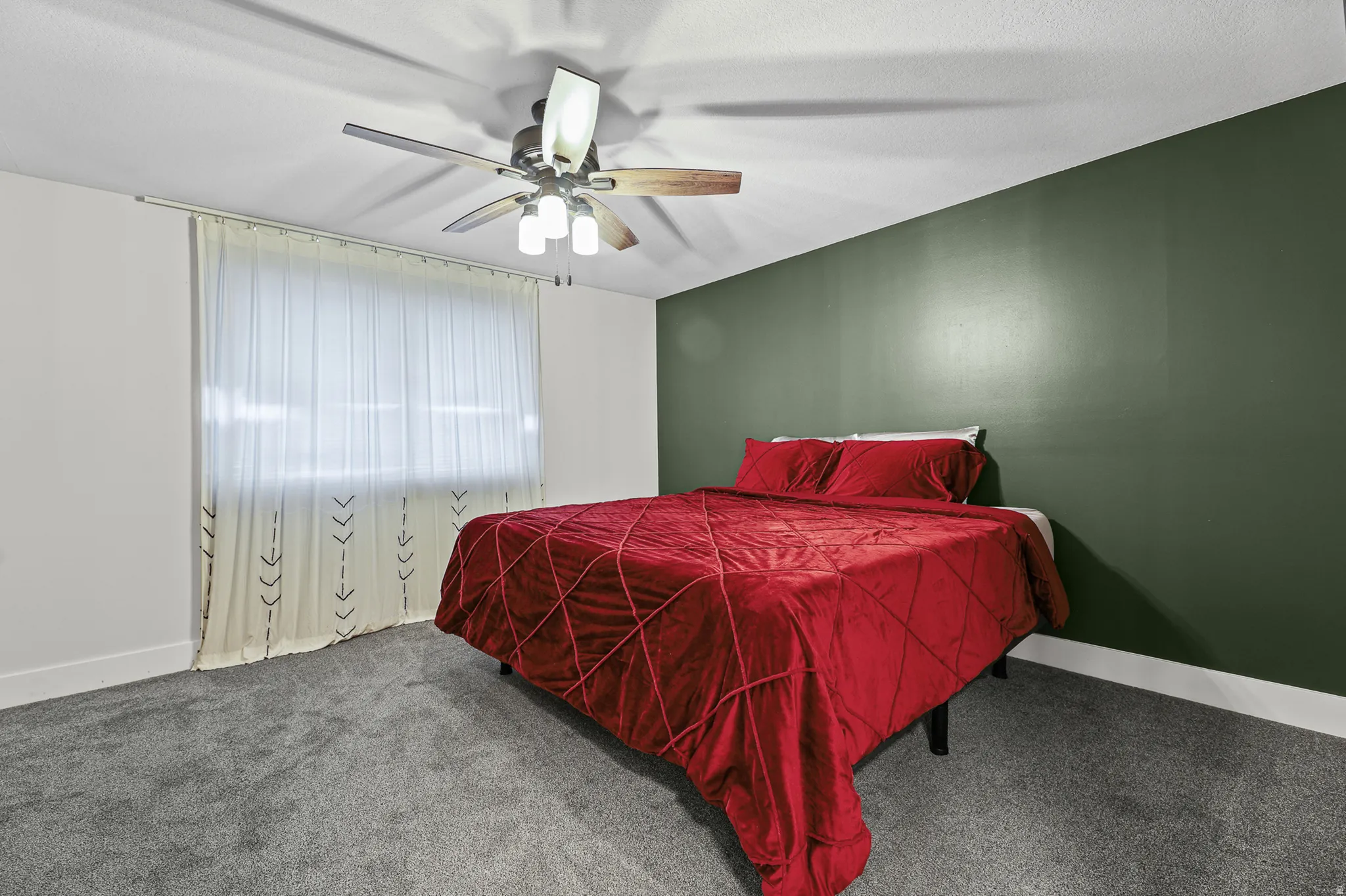 Large bedroom featuring a full wall of deep green accent paint, and a multi-speed ceiling fan with integrated lighting