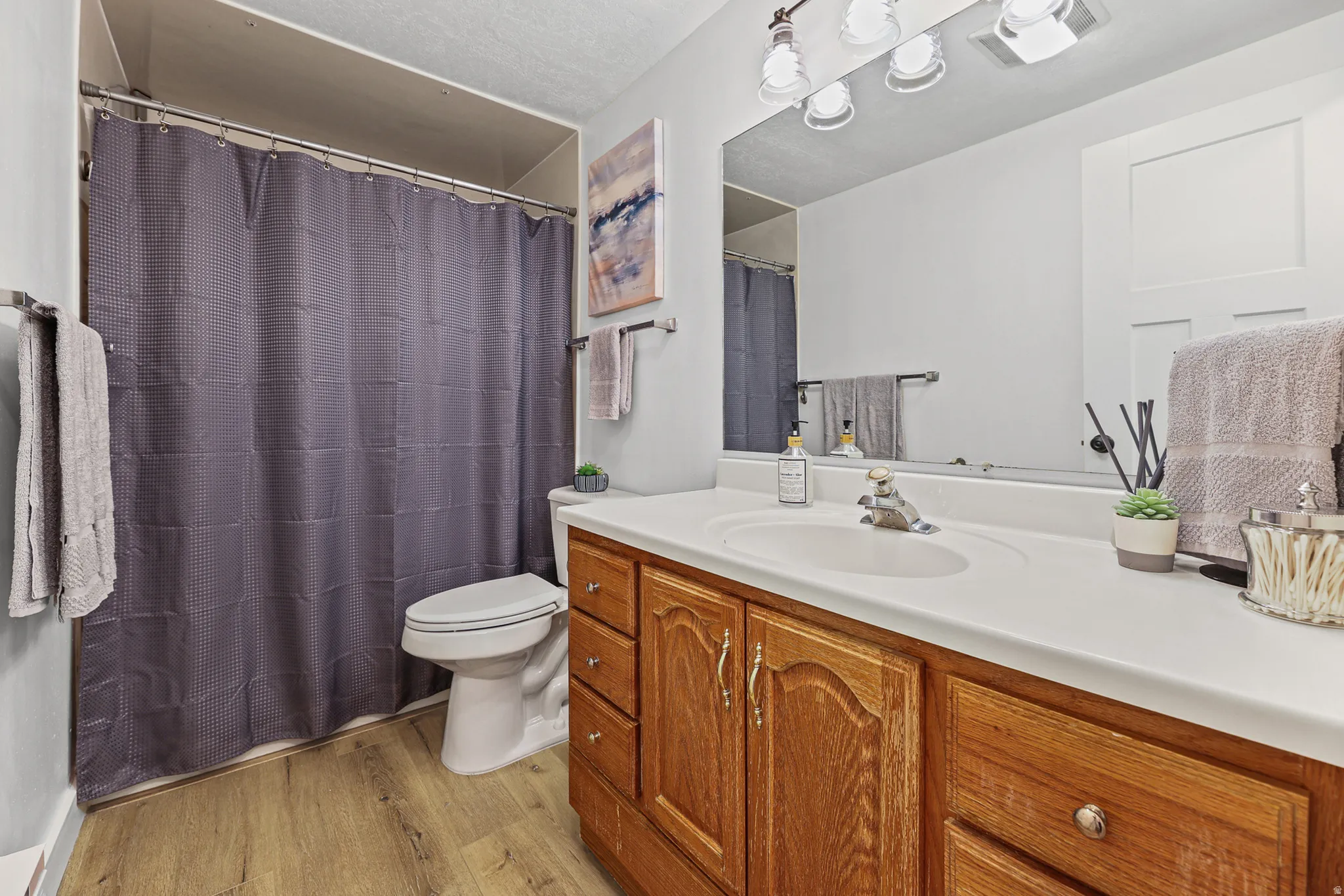 Bathroom featuring a wood-finish vanity with a white countertop and integrated sink, a large wall-mounted mirror, and overhead vanity lighting