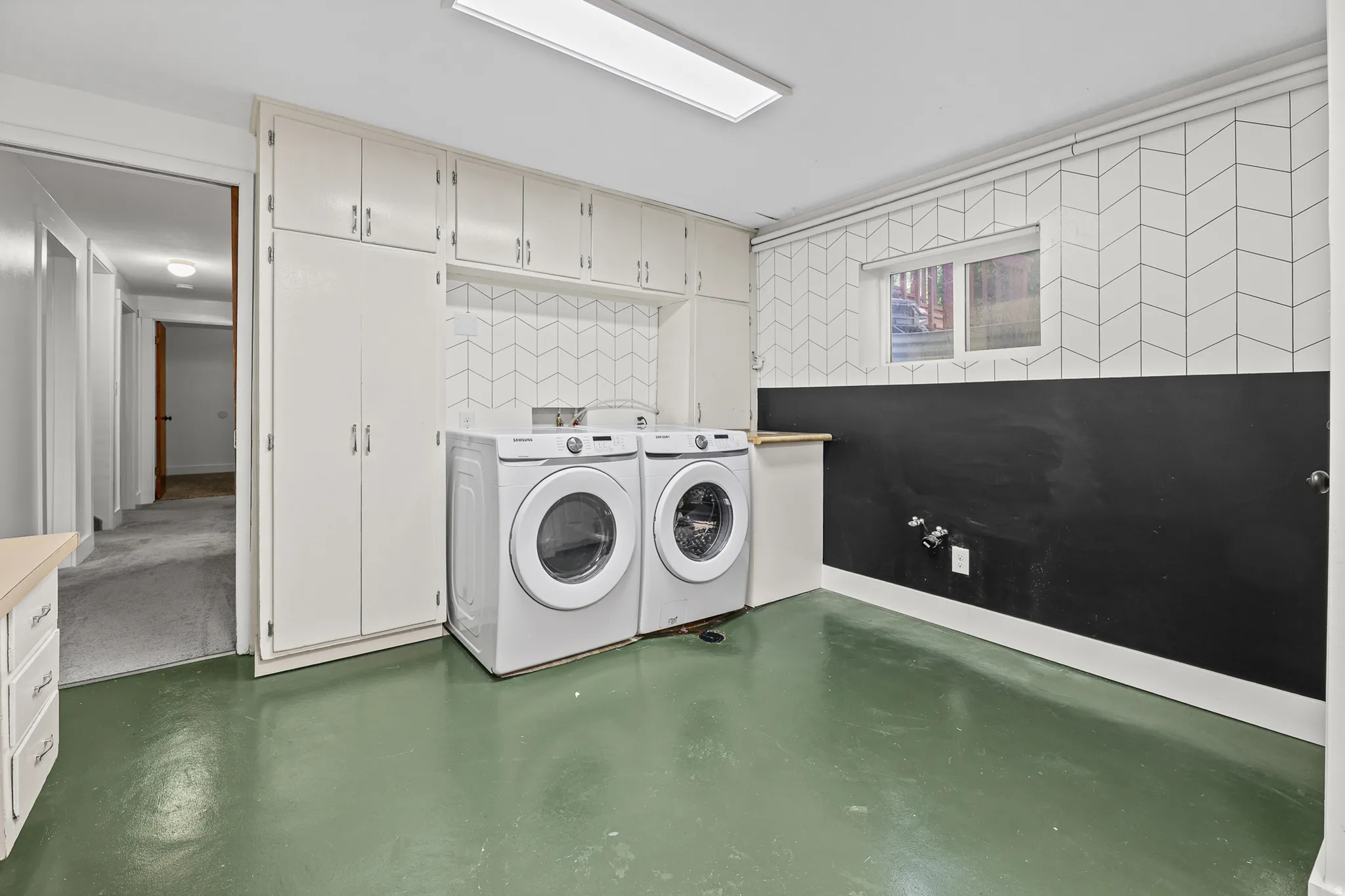 Dedicated utility area featuring extensive built-in cabinetry, a geometric pattern accent wall, a contrasting lower wall, a window, and durable flooring