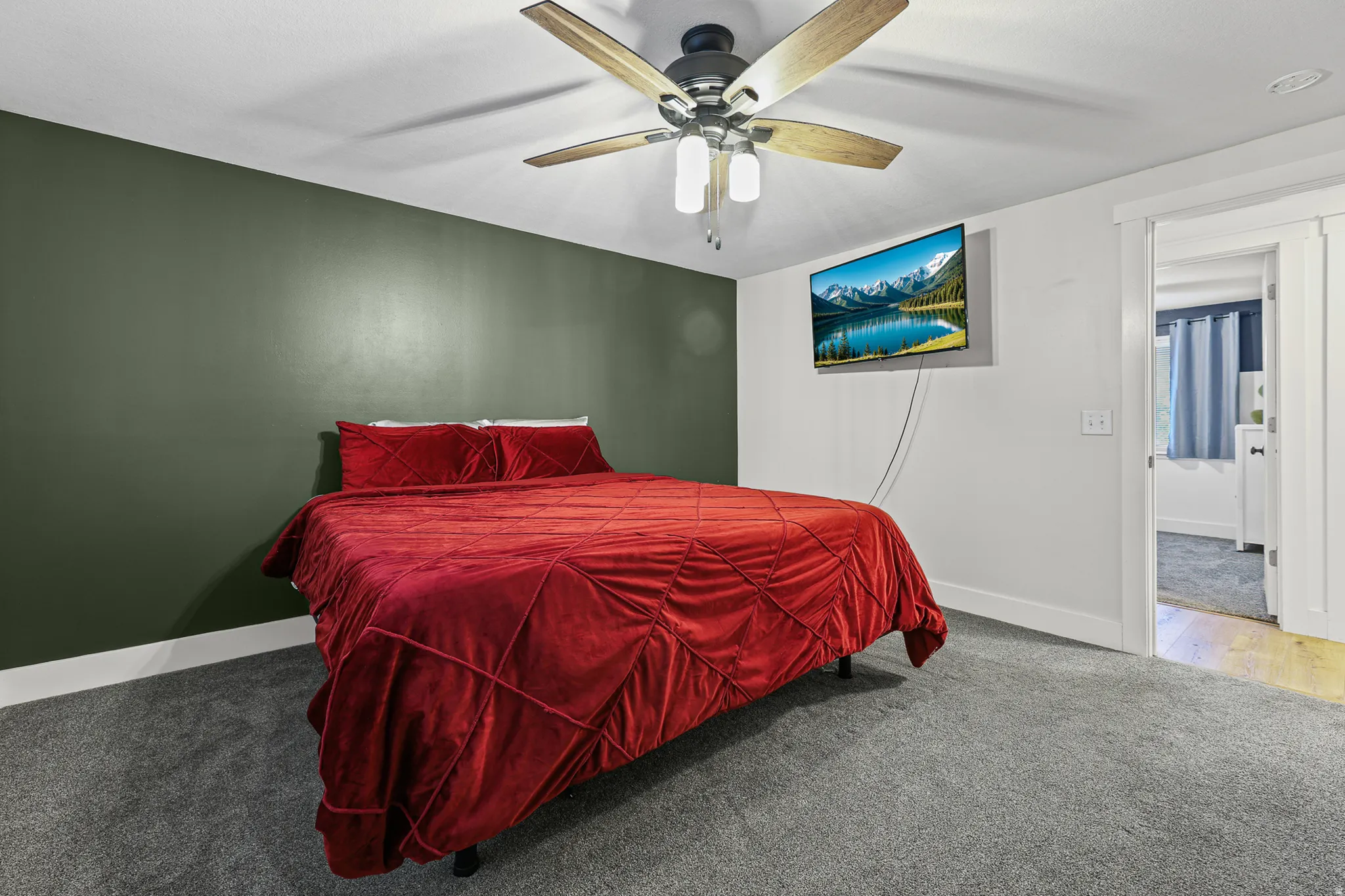Bedroom featuring a ceiling fan with light fixture, rich green accent wall, and gray carpet