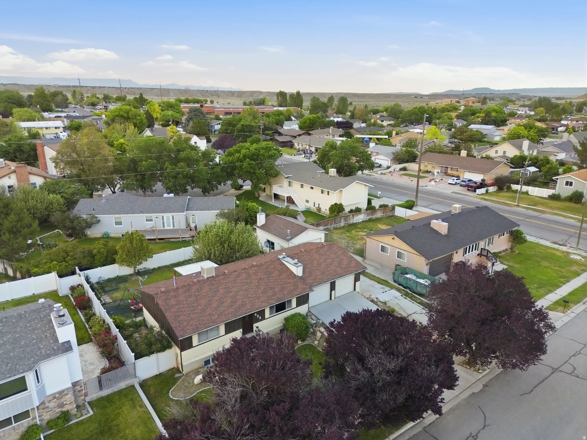 Residential aerial view of the neighborhood featuring a paved street, mature trees, and single-family homes.