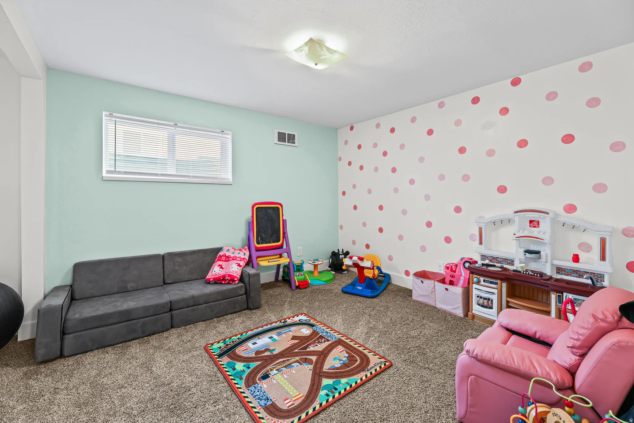Carpeted room featuring a window with horizontal blinds, light blue painted walls, and a white wall with red and pink polka dot accents