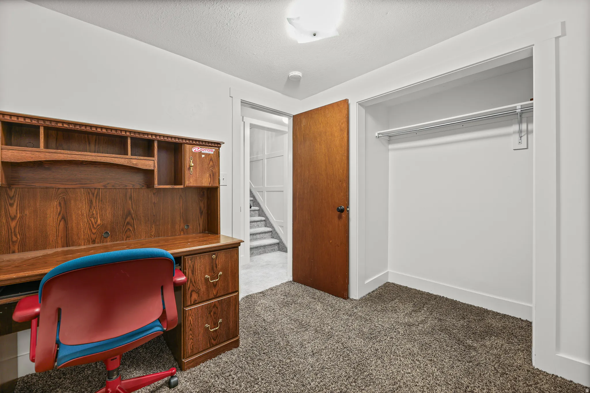Carpeted room featuring a built-in closet with a hanging rod, white trim, and a warm wood-finish door