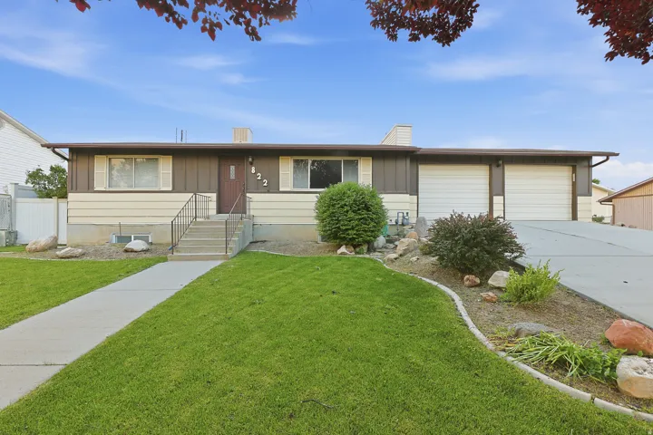 Ranch-style residence featuring a two-tone exterior, a concrete walkway leading to the front entry, a two-car garage, and established landscaping with decorative rocks