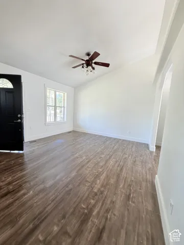Open-concept living space with wood-finish flooring, vaulted ceilings, and a ceiling fan with integrated lighting