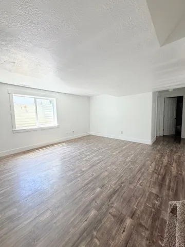 Spacious room featuring wood-finish flooring, white baseboards, and a window with a window well