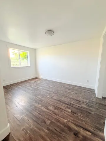 Spacious interior room featuring wood-finish flooring, white baseboards, and a neutral wall palette