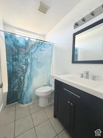Bathroom featuring a black vanity with a white countertop and integrated sink, chrome faucet, wall-mounted mirror, and tile flooring