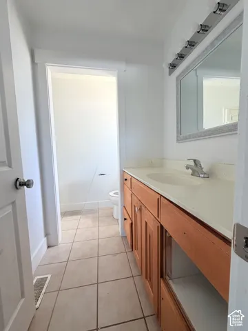 Bathroom vanity featuring wood-finish cabinetry, a single basin sink, and a light-colored countertop
