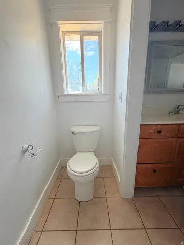 Bathroom featuring a window with white trim, a white toilet, and neutral-toned tile flooring