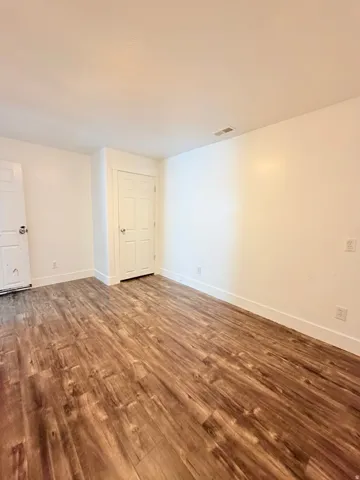 Spacious room featuring wood-finish flooring, white walls, and white trim