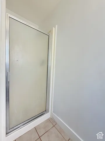 Enclosed shower stall with a frosted glass door and a metal frame, set on light-toned tile flooring