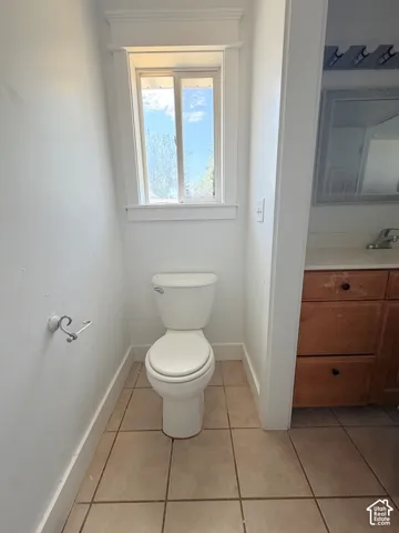 Compact half-bath featuring a white toilet, tile flooring, and a single window with white trim
