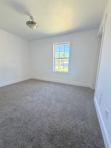 Bright room featuring a window with white trim, gray carpet flooring, white walls, and a ceiling-mounted light fixture