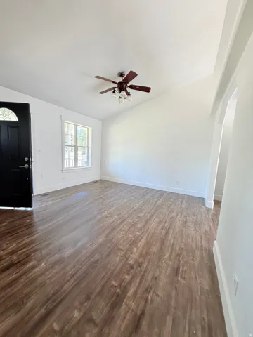 Open-concept living space with wood-finish flooring, vaulted ceilings, and a ceiling fan with integrated lighting